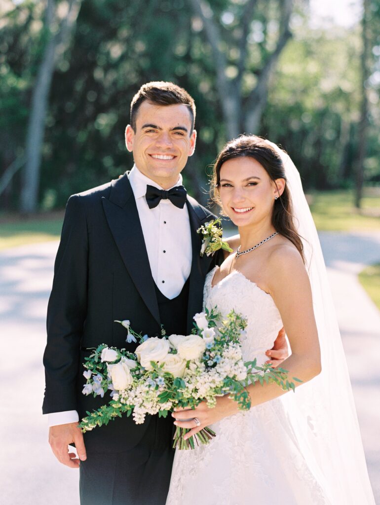 Groom in tuxedo and bride holding white, blue and purple bridal bouquet